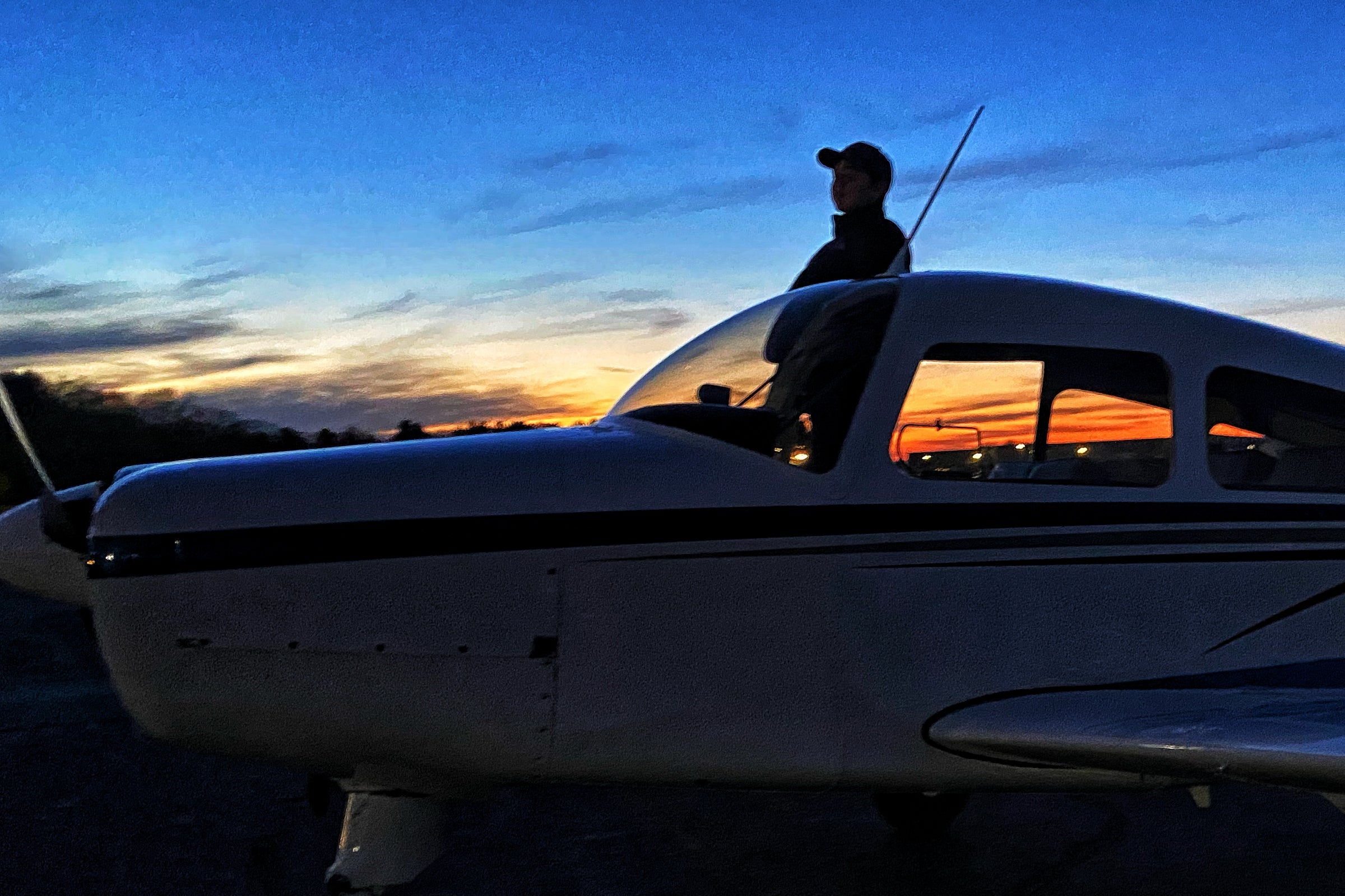 Teen pilot standing on wing of parked single engine plane at sunset.